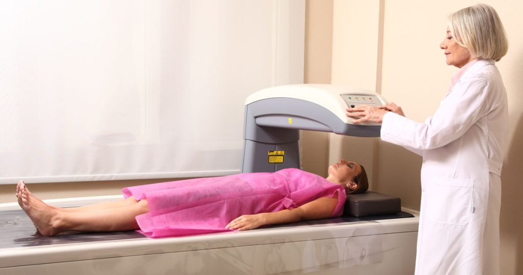 DEXA scan. Woman lying on the bed and technician scans bone density with the DXA scanner.